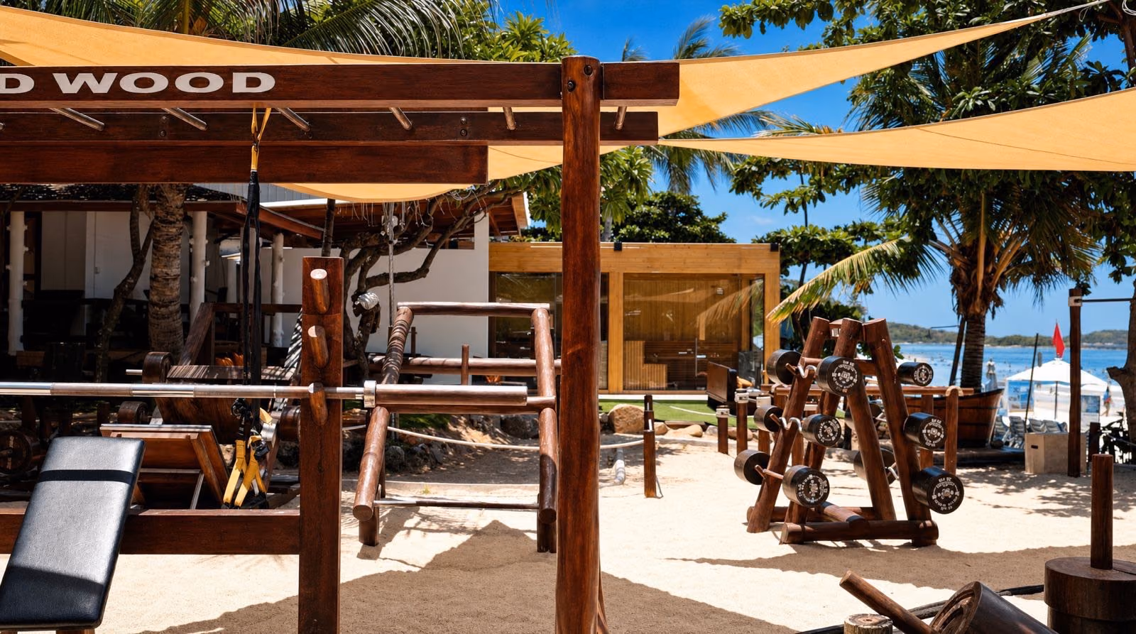 Wild Wood's wooden rigs on the sand, the sauna cabin behind them and the sea beyond — the whole circuit in one corner of the beach